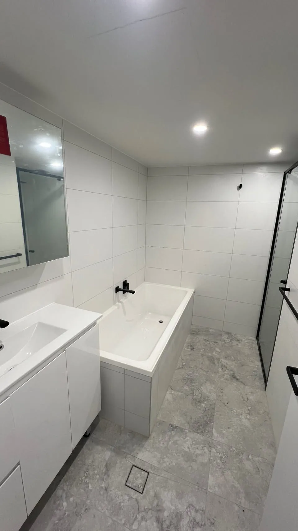 White freestanding bath with black tapware against terrazzo tiles