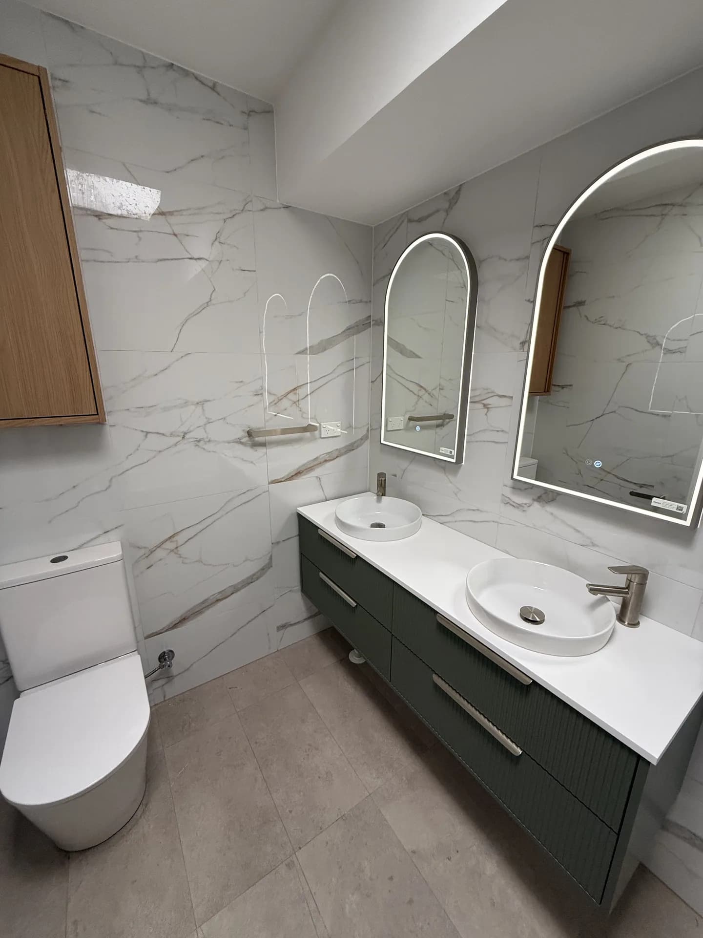 Renovated Drummoyne apartment bathroom with marble-look tiles, green fluted double vanity and twin arched mirrors